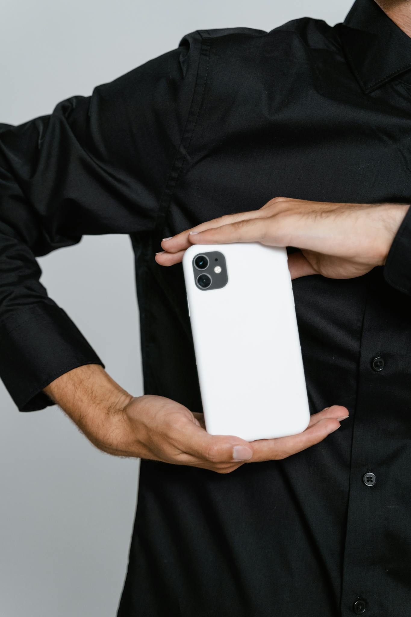 Close-up of a man holding a white smartphone against a black shirt in studio lighting.