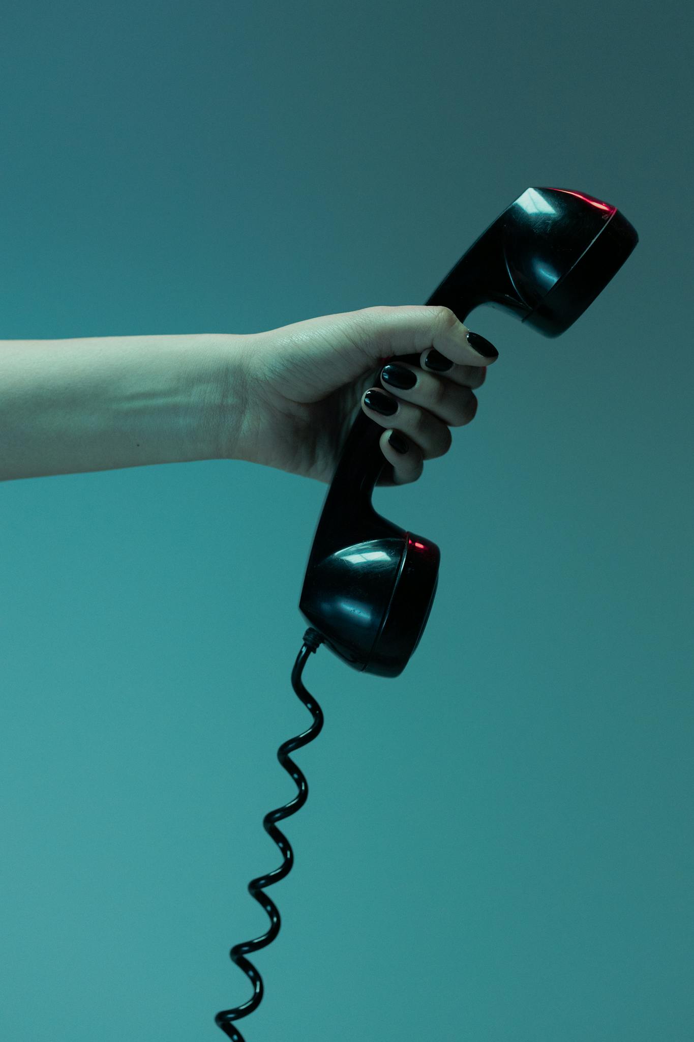 Moody close-up of a hand holding a vintage telephone receiver against a blue background.